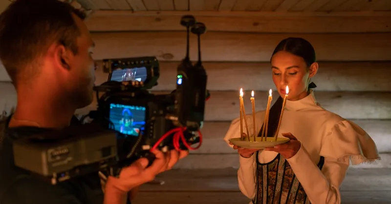 A filmmaker captures a woman holding candles in a dramatic indoor setting.