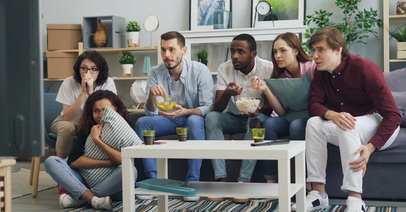 Group of friends watching a thriller movie at home, sharing snacks and reactions.