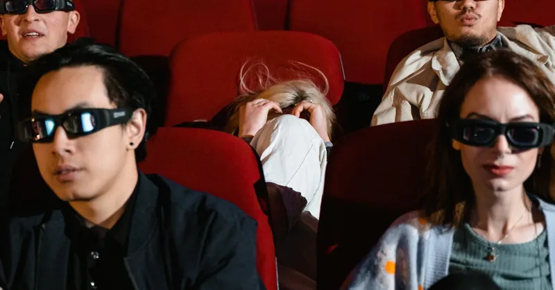 People wearing 3D glasses watch a film in a movie theater, displaying various expressions.