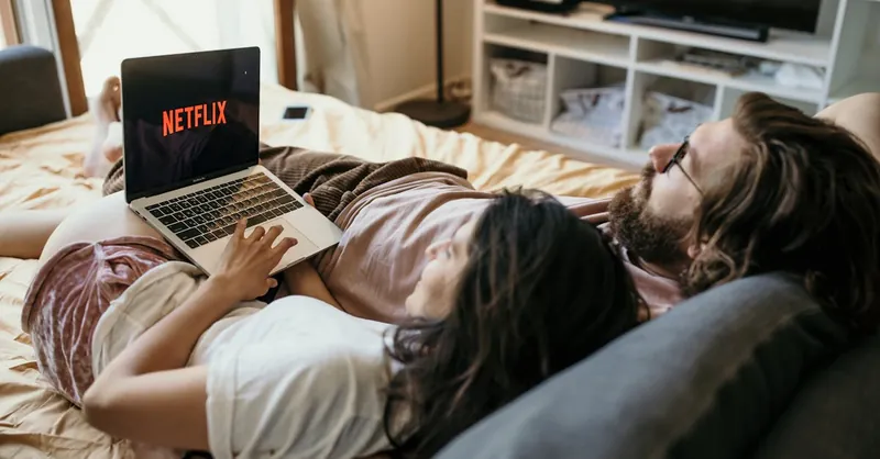 A cozy couple lounging in bed, streaming Netflix together on a laptop, enjoying a peaceful moment.