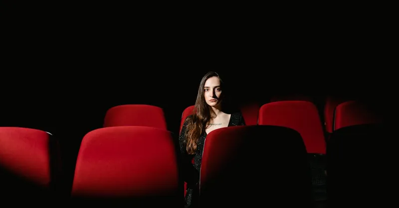 A single woman sits alone in a dimly lit cinema theater, evoking solitude and introspection.
