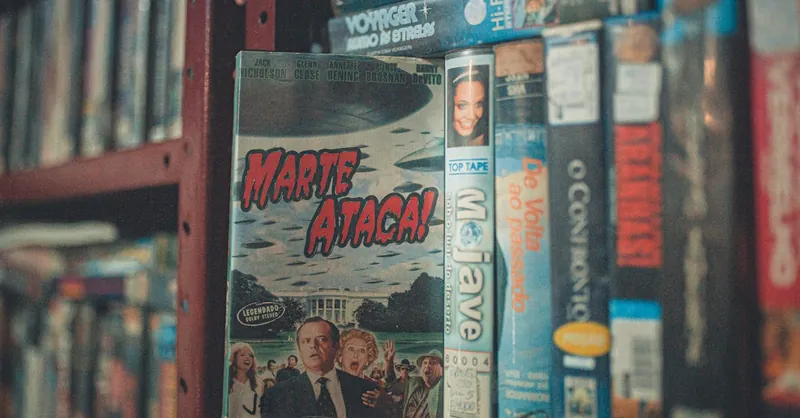 A nostalgic display of vintage VHS tapes with classic movie titles on a wooden shelf indoors.