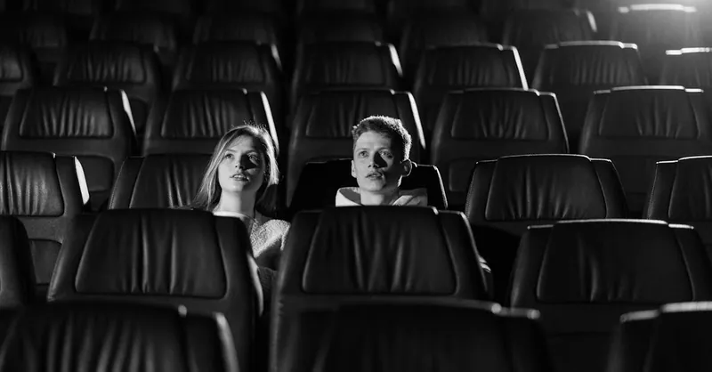 A couple watching a movie in an empty theater with monochrome lighting.