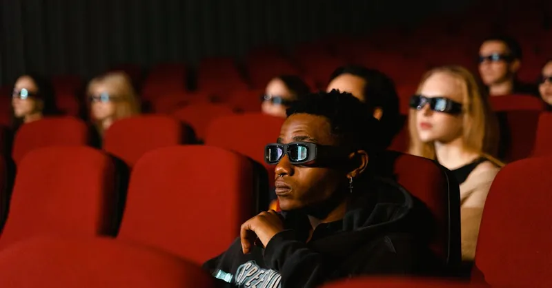 A diverse group of people wearing 3D glasses enjoying a movie in a cinema with red seats.