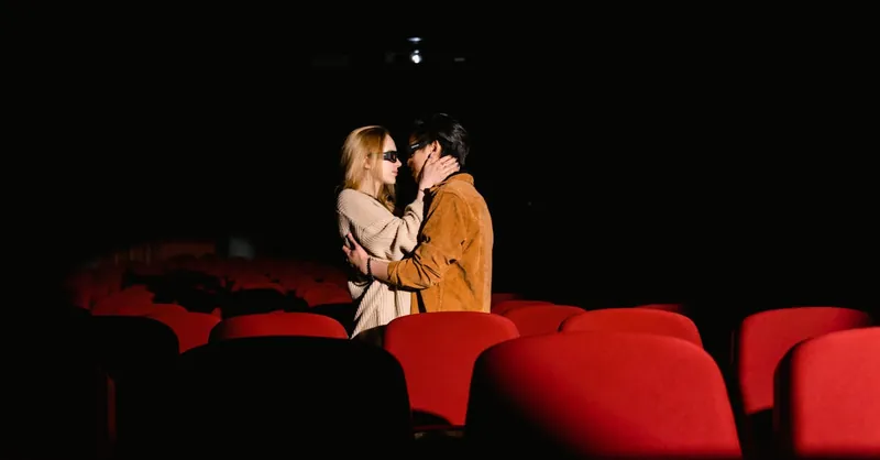Couple sharing a tender moment in an empty movie theater with red seats.