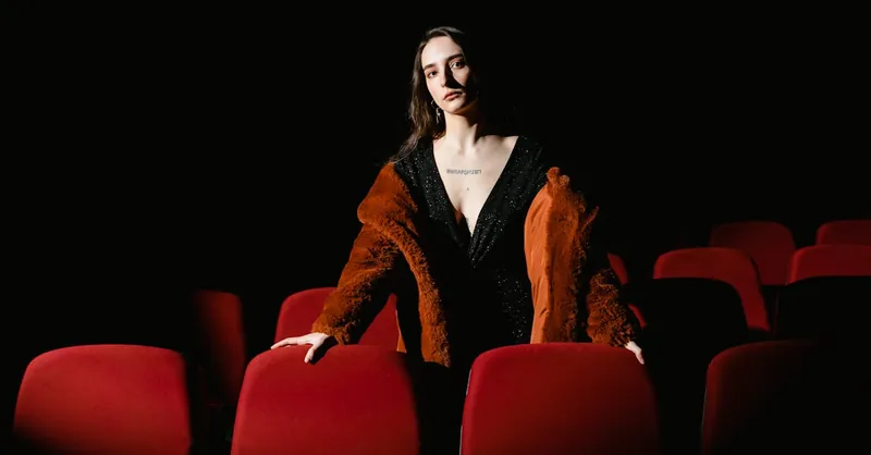 Stylish woman in a coat stands in an empty cinema with red seats, exuding elegance.
