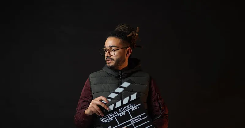 A filmmaker holding a clapperboard against a black background, emphasizing cinematic creativity.