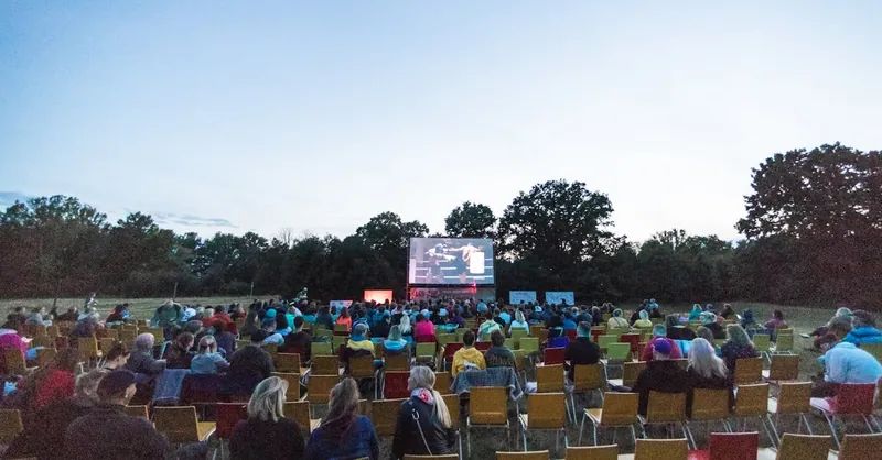 A large audience enjoys an outdoor movie screening in a Czech park at twilight.