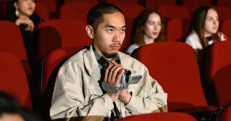A man with a camcorder sits in an empty theater, focused and attentive.