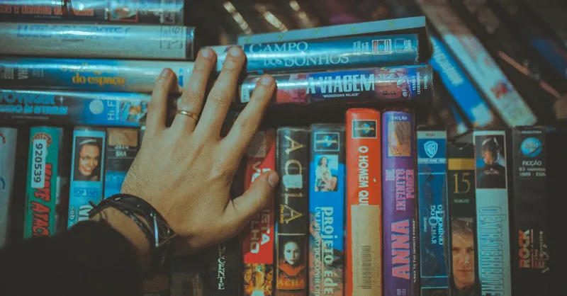 A hand reaching for a classic VHS tape from a colorful vintage collection indoors.
