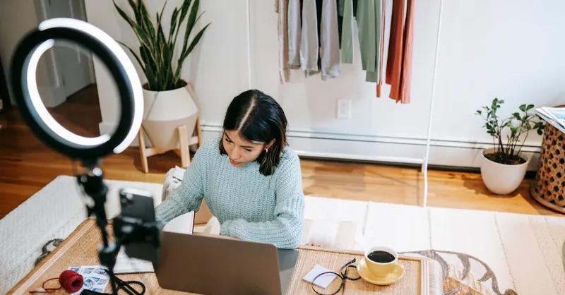 Young woman working at home office with laptop, coffee, and lighting equipment.