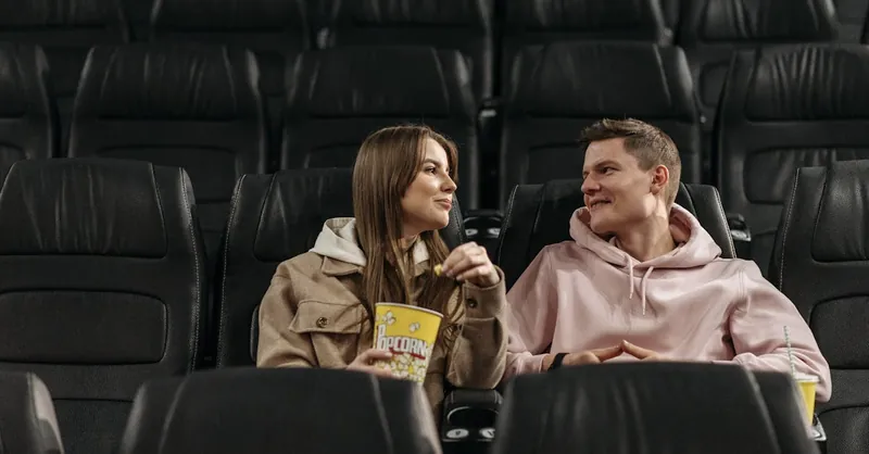 A couple sits in an empty cinema, enjoying popcorn and conversation in a cozy setting.