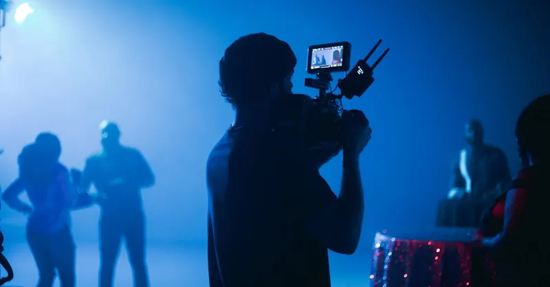 Behind-the-scenes image of a film crew and actors in a cinematic setting with dramatic lighting.