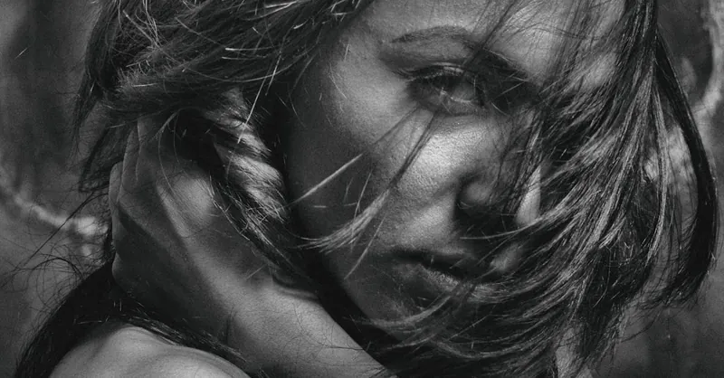 Intense black and white portrait of a woman with hair in motion, captured with dramatic lighting.
