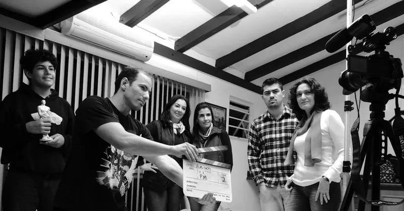 A group of adults collaborate on a filmmaking project, seen holding a clapperboard indoors.