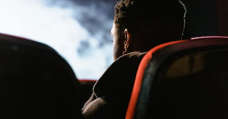 A person sits in a theater watching a movie on a large screen, enveloped in a dark ambiance.