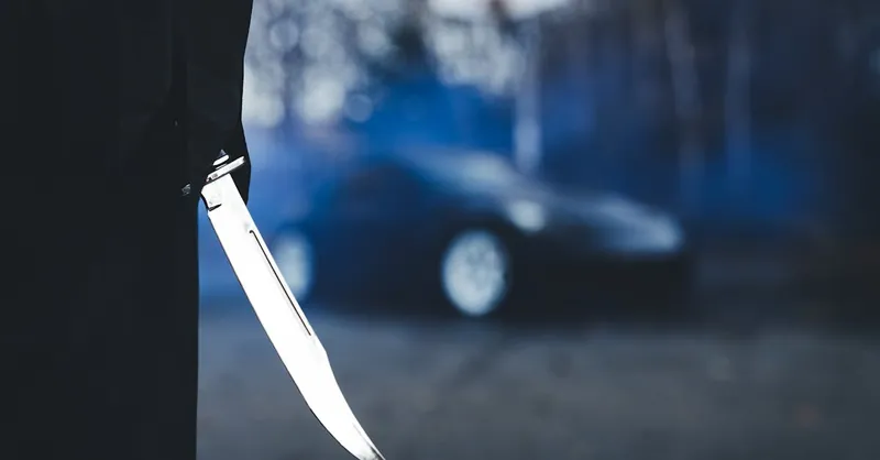 Close-up of a knife with a blurred car in the background, creating a tense atmosphere.