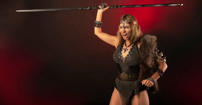A powerful image of a female warrior in costume wielding a sword, captured in a dramatic studio setting.